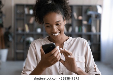 Happy Black millennial gen Z girl flirting on dating website, getting good news, reading text, using app on smartphone, browsing internet on mobile phone, smiling, laughing at joke. Digital life - Powered by Shutterstock