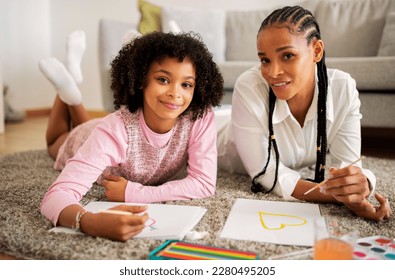 Happy Black Mom And Daughter Drawing Painting Together Using Watercolor Lying On Floor At Home, Smiling To Camera Enjoying Time Together. Family Weekend Leisure, Hobby Concept - Powered by Shutterstock