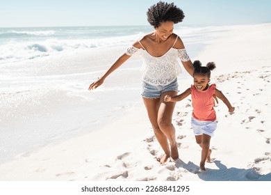 Happy black mom with daughter running on summer beach with copy space. Cheerful african american mother running along seaside with cute little girl. Happy older sister having fun with kid at ocean. - Powered by Shutterstock