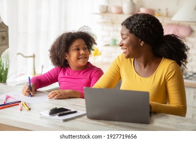 Happy Black Mom And Her Little Daughter Spending Time Together In Kitchen, Cute Preschool Girl Drawing At Table While Her Mom Working Remotely On Laptop Computer At Home, Free Space