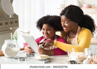 Happy Black Mom And Little Daughter Using Digital Table In Kitchen Together, Checking Recipe Of Dough Online While Preparing Pastry, African American Family Cooking At Home And Having Fun , Free Space