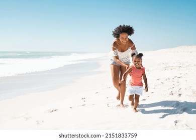 Happy black mother with cute little girl running barefoot on white tropical beach. Cheerful african american woman running along beach with her cute little sister. Smiling mother and funny female kid. - Shutterstock ID 2151833759
