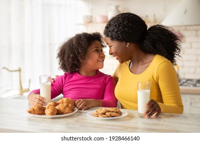 Happy Black Mother And Daughter Bonding Together While Having Snacks In Kitchen, Cheerful African American Mom And Her Little Child Sitting At Table Eating Cookies And Drinking Milk, Free Space