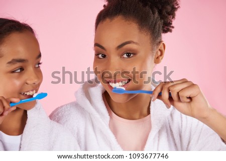 Happy black mother and daughter in dressing gown brush teeth. Dental hygiene concept. Isolated on pink background. Studio portrait.