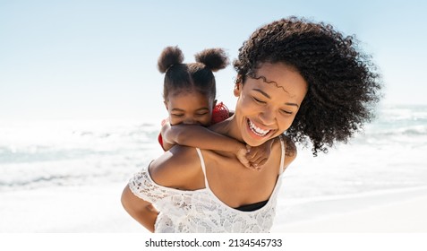 Happy black mother giving piggyback ride to her daughter at beach while laughing. Close up of beautiful and carefree mom carrying on shoulders her kid. Cute african little girl with bigger sister play - Shutterstock ID 2134545733