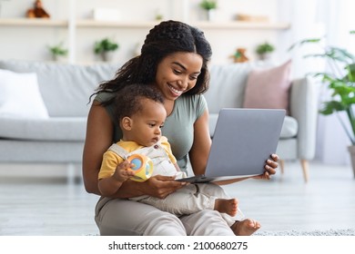 Happy Black Mother And Her Little Infant Son Using Laptop Computer At Home, Smiling African American Mom Showing Cartoons To Toddler Child While Relaxing On Floor In Living Room Together, Free Space