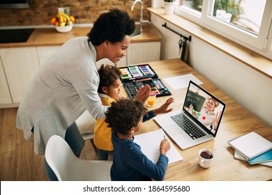 Happy black mother and kids waving to a teacher while having video call over a computer from home. 