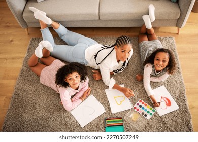 Happy Black Mother And Two Daughters Drawing Together Lying On Floor In Modern Living Room At Home On Weekend  Smiling To Camera  Family Hobby And Leisure  Above View Shot