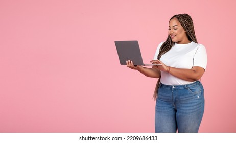 Happy Black Obese Woman Using Laptop Computer Websurfing And Working Online Posing Standing On Pink Background. Internet Technology Business And Freelance Career. Panorama With Empty Space