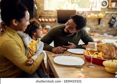 Happy Black Parents And Their Small Daughter Having Thanksgiving Lunch And Communicating At Dining Table.