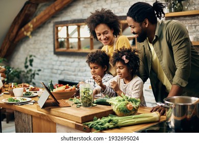 Happy black parents and their small kids preparing healthy meal in the kitchen. 