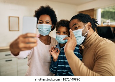 Happy Black Parents And Their Son Having Fun While Taking Selfie With Mobile Phone And Wearing Face Masks Due To Coronavirus Pandemic.