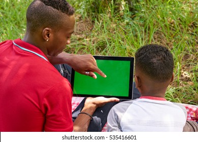 Happy Black People In City Park. African American Family With Young Man And Child Using Tablet Computer For Internet. Laptop Monitor With Green Screen