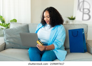 Happy Black Plus Size Woman Shopping Via Laptop And Credit Card Buying New Clothes And Making Online Payment Sitting On Sofa At Home. Internet Banking And Ecommerce Concept