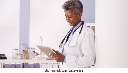 Happy Black Senior Doctor Standing In Office With Tablet