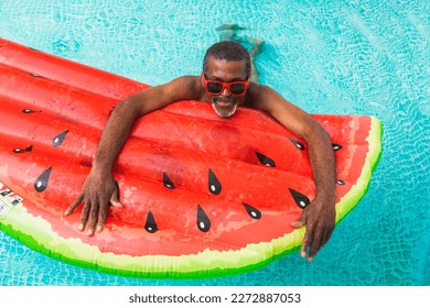 Happy black senior man having party in the swimming pool - Active elderly male person sunbathing and relaxing in a private pool during summertime - Powered by Shutterstock