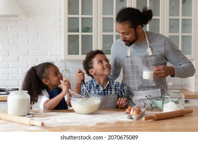 Happy Black Sibling Kids And Young Dad Wearing Aprons, Cooking Bakery Food For Family Dinner Together. Father Teaching Kids To Bake, Mixing Dough In Bowl For Pastry, Use Flour, Milk, Eggs, Whiskers