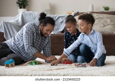 Happy Black Sibling Kids And Young Dad Playing On Warm Carpeted Floor In Comfortable Living Room, Relaxing At Home, Building Toy Road, Driving Transport, Playing Creative Games Together. Fatherhood