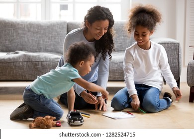 Happy black single mom   2 mixed race kids draw and colored pencils warm floor together  african mother baby sitter helps children son daughter playing having fun at home  creative family hobby