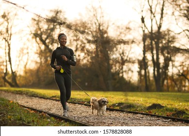 Happy Black Sportswoman Running With Her Dog At The Park.  