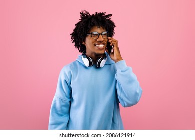 Happy Black Teenager With Headphones Talking On Smartphone On Pink Studio Background. Positive African American Teen Guy Making Phone Call, Smiling And Having Friendy Conversation