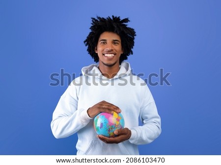 Happy black teenager protecting globe with his hands on blue studio background. Environmental protection, ecology, international tourism, equality of mankind, tolerance for others concept