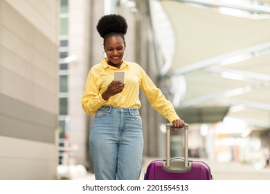 Happy Black Tourist Woman Using Smartphone Standing With Suitcase Booking Travel Tickets Via Mobile Application At Airport Terminal Outdoor. Tourism And Gadgets Concept - Powered by Shutterstock