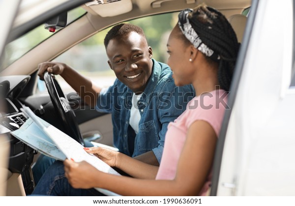 Happy black travellers reading map while\
having car trip together, got lost in the middle of road, side\
view, copy space. Smiling african american young man and woman\
looking for new\
destination