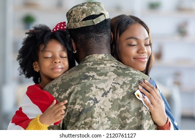 Happy Black Wife And Little Daughter Embracing Soldier Father At Home, Loving Family Welcoming Military Man In Camouflage Uniform After Returning From Us Army, Celebrating Reunion, Closeup