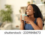 Happy black woman breathing drinking coffee sitting at home