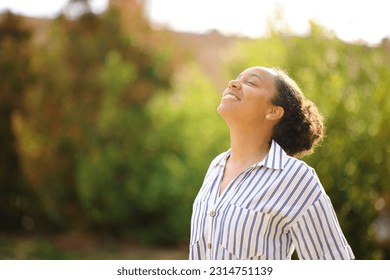 Happy black woman breathing fresh air standing in a park