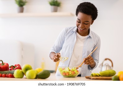 Happy Black Woman Cooking Healthy Food, Dressing Vegetable Salad With Oil Standing In Kitchen At Home. Nutrition And Health, Recipes For Weight Loss And Dieting Concept. Selective Focus