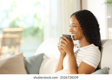 Happy black woman drinking coffee smiling sitting on a couch at home - Powered by Shutterstock