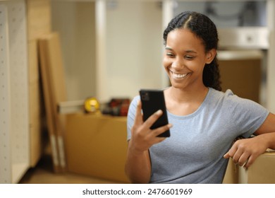 Happy black woman moving home checking phone  in the kitchen - Powered by Shutterstock