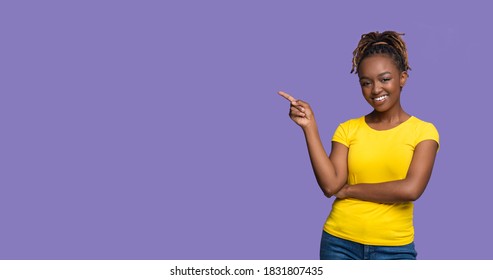 Happy Black Woman Pointing At Copy Space Over Purple Studio Background, Panorama. Young Pretty African American Lady Smiling And Indicating To Empty Space For Text Or Advertisement