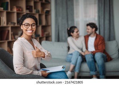 Happy black woman psychologist in glasses show thumb up, smiling millennial european man looking at wife at doctor consultation in clinic office interior. Professional help, family therapy and support - Shutterstock ID 2167421805