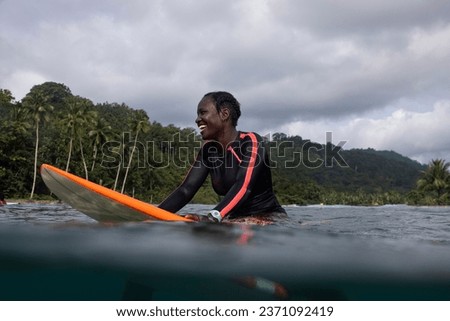 Happy black woman surfer floating on her surfboard and smiling happily waiting for a wave and enjoying the surfing lifestyle in Sao Tome and Principe, Africa
