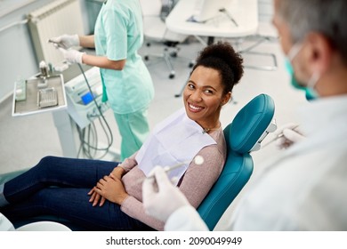 Happy Black Woman Talking To Her Dentist During Dental Exam At Dentist's Office.