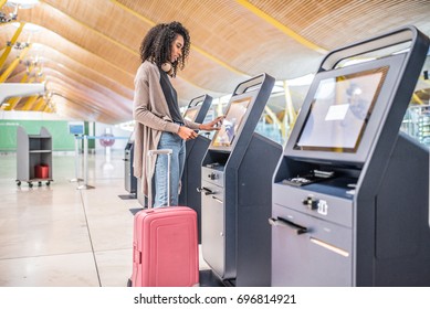happy black woman using the check-in machine at the airport getting the boarding pass.