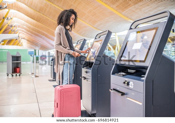 happy black woman using the check-in\
machine at the airport getting the boarding\
pass.