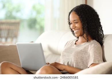 Happy black woman using laptop sitting on a couch at home - Powered by Shutterstock