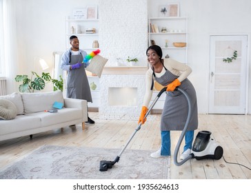 Happy Black Woman Vacuuming Floor While Her Boyfriend Dusting Cushion At Their Apartment, Copy Space