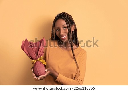 happy black young woman celebrating easter egg gift in beige studio background. holiday, easter, celebration concept.