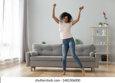 Happy black young woman have fun dancing alone in living room at home, overjoyed african American millennial girl move to rhythm enjoy weekend listen to music on cellphone. Stress free concept