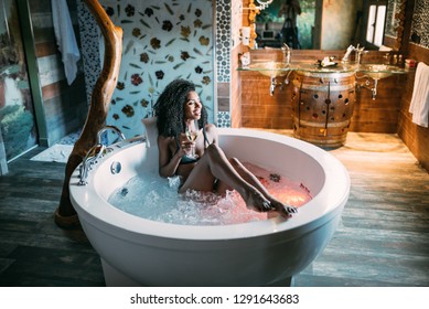 Happy black young woman relaxing in the hydro massage bath drinking wine