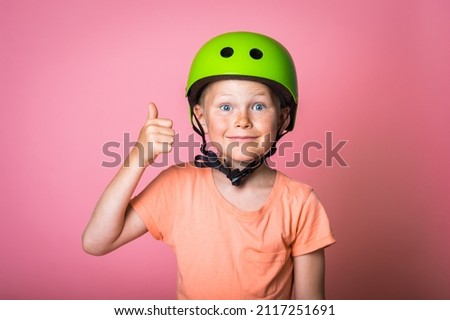 Happy blond kid boy in green helmet isolated on pink background. Child make big eyes and thumb up. Winner . Number one.
