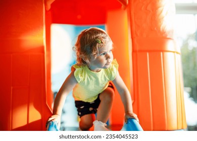 Happy blond little toddler girl having fun and sliding on indoor playground at daycare or nursery. Positive funny baby child smiling. Healthy girl climbing on slide. - Powered by Shutterstock