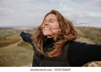 A happy blond woman with brown hair, arms outstretched, enjoying the nature outdoors. The happy woman is smiling, embracing the wind, and feeling free in nature. Happy woman outdoors in nature.