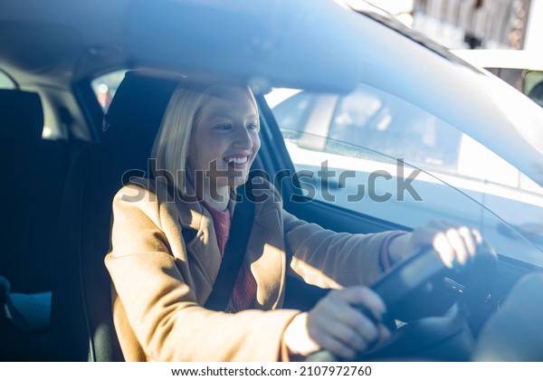 Happy blond woman driving a\
car. Portrait of beautiful caucasian woman with toothy smile\
driving car. Hand on steering wheel. Young woman driving a car in\
the city
