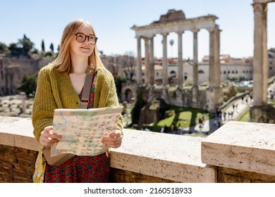 A happy blond woman tourist is standing near the Roman Forum, old ruins at the center of Rome, Italy. Concept of traveling famous landmarks. Girl with map is walking on a sunny day